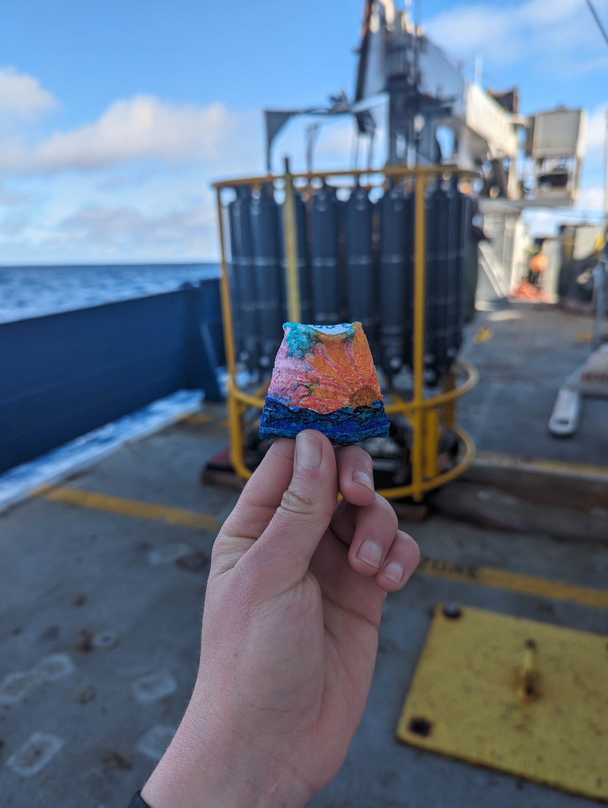 shrunken cup held up in front of the CTD on deck