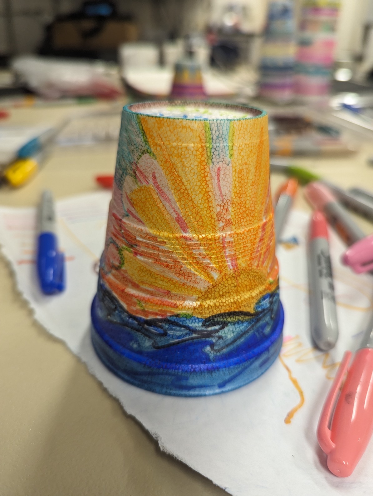 sunset drawn on styrofoam cup, more cups and art supplies in background of photo