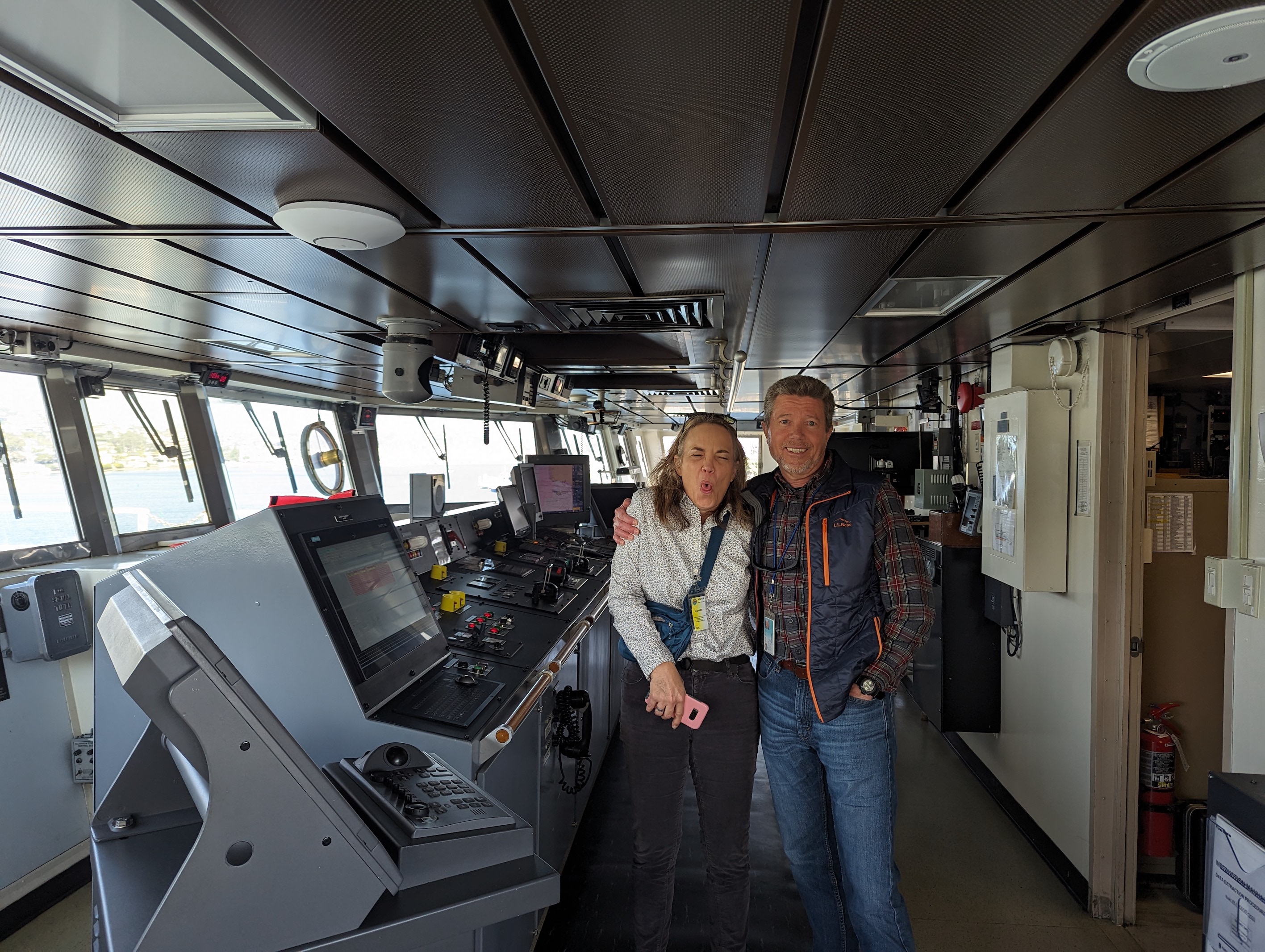 Two adults, Caro's parents, standing on the bridge of a ship, surrounded by navigational controls