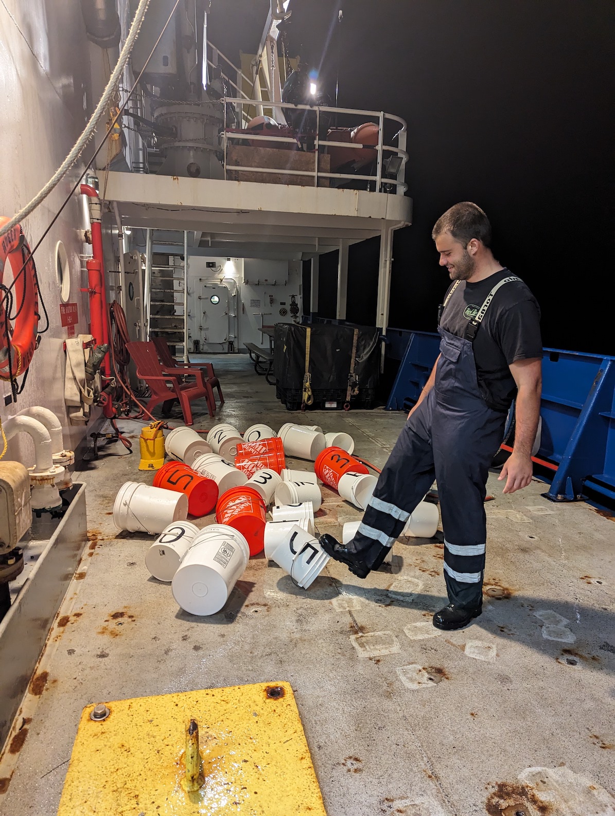 Sam standing around with a pile of buckets on the deck of the ship