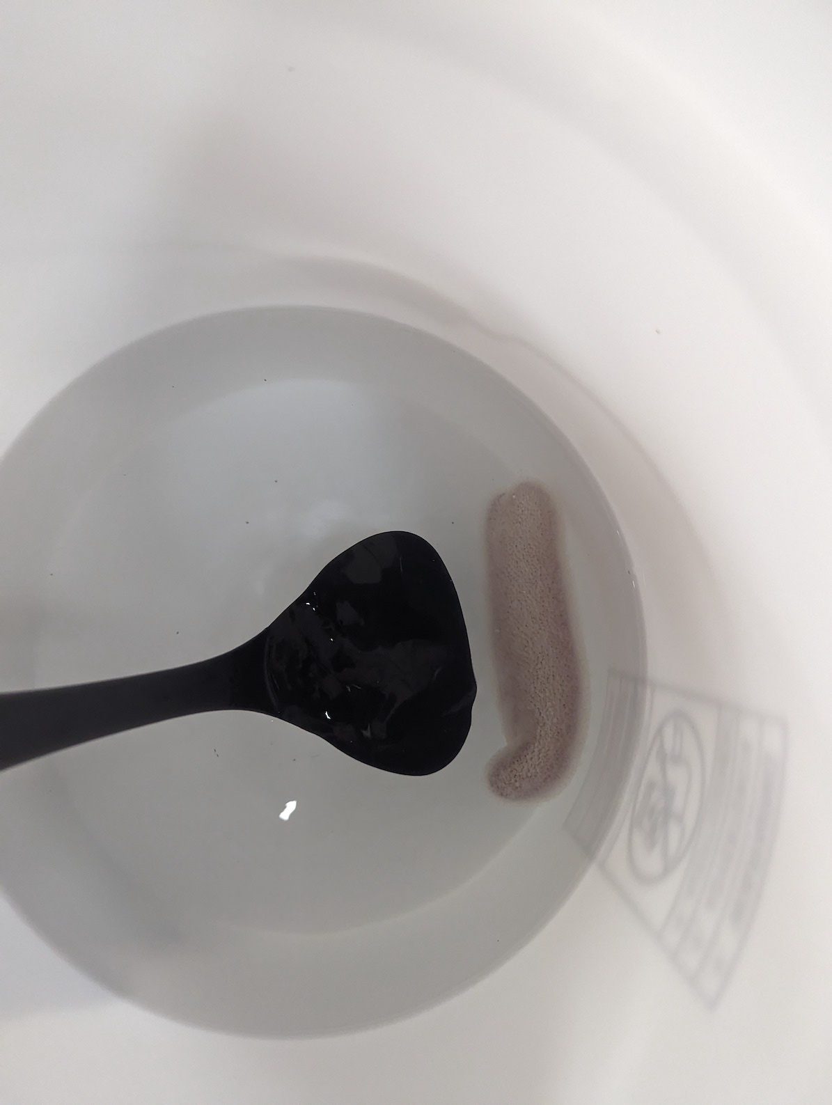 a thick pyrosome in a white bucket, being held by a black ladle