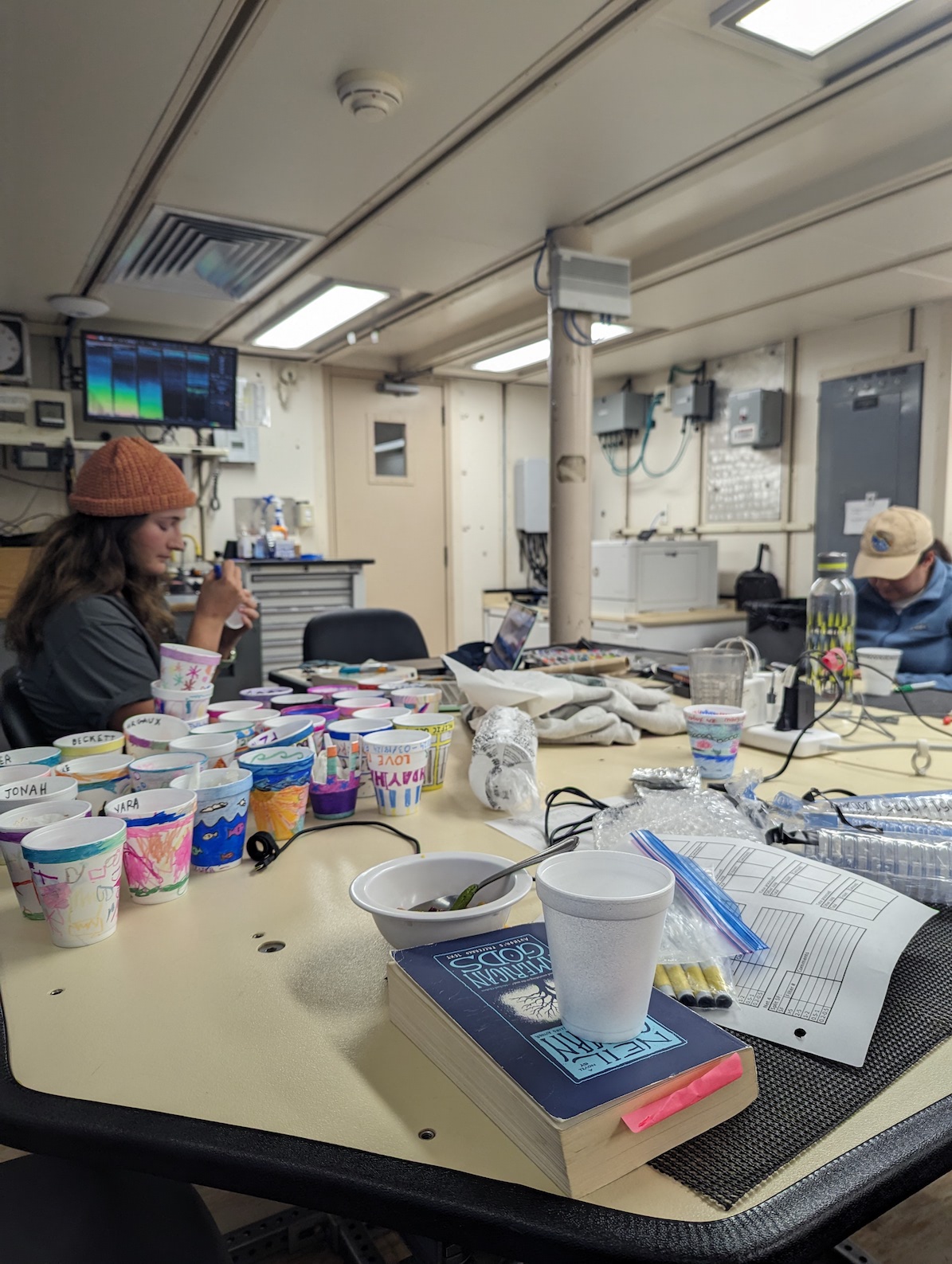 several people coloring cups surrounded by other decorated cups in a computer lab