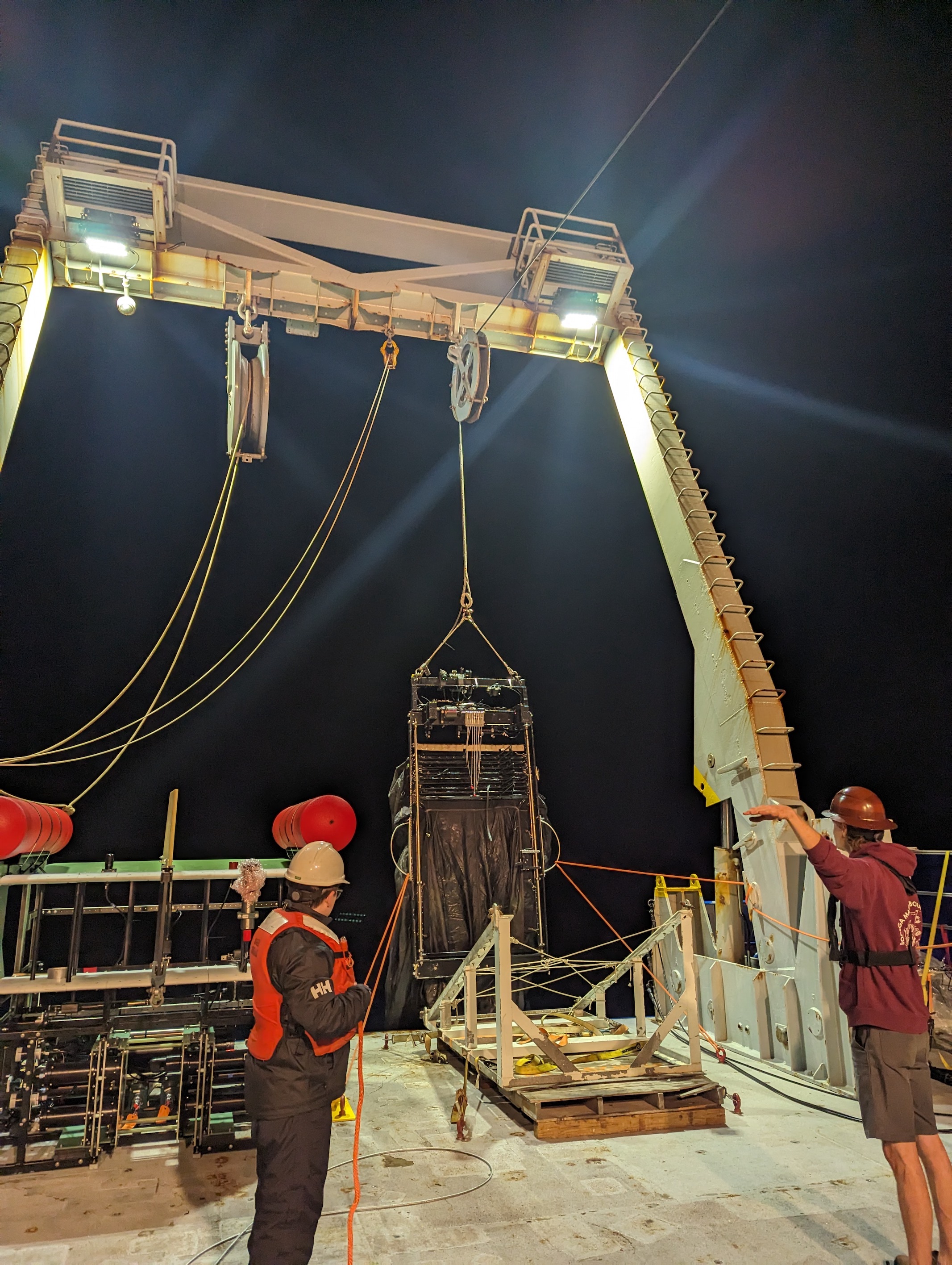 Net being lifted into the water, off the back of a ship. two people in image, one guiding the winch and other manning a tag line.