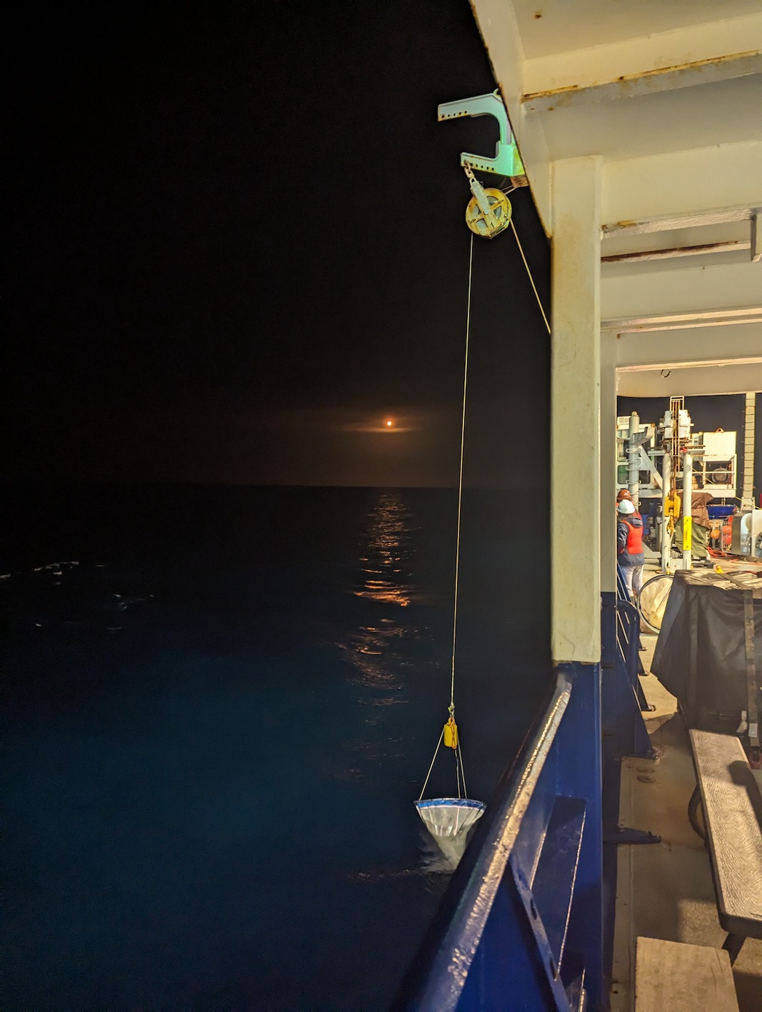 orange glow from rocket in the background, with a salp net being lowered into the ocean