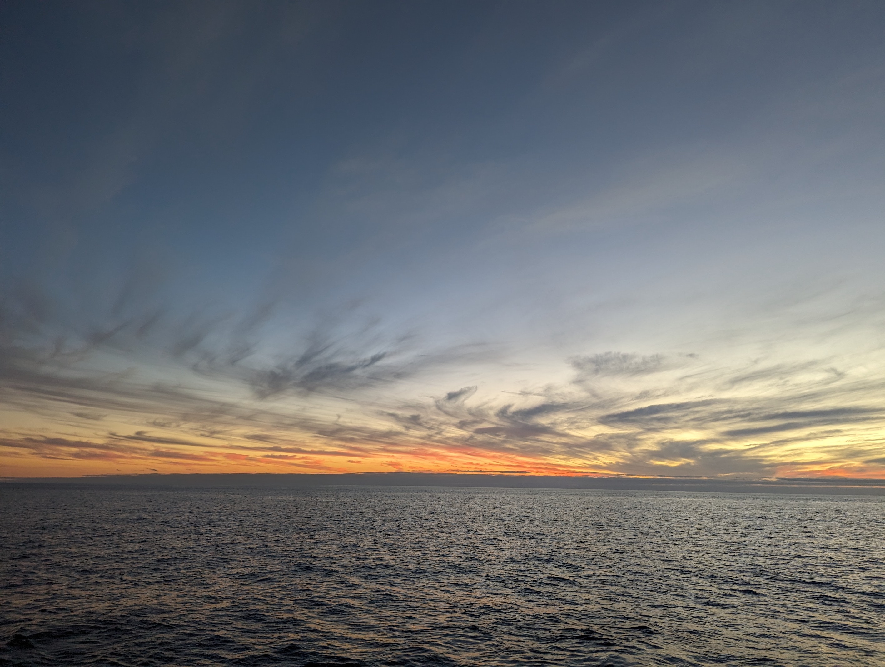 image of sunset over the ocean, with streaky clouds.